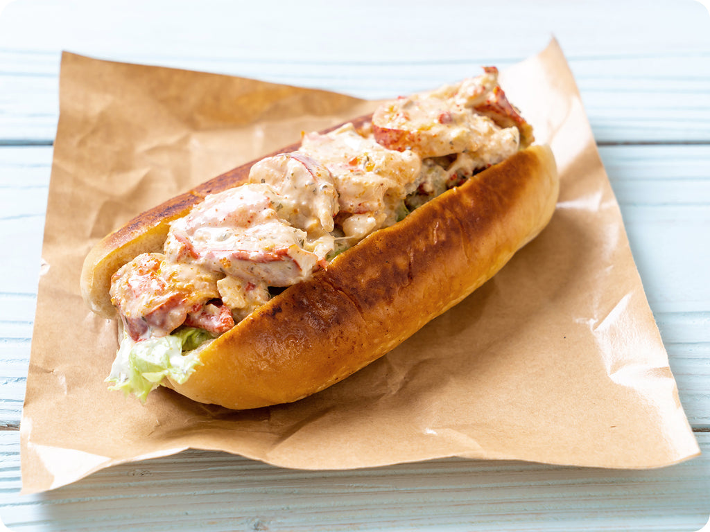 Classic lobster roll in a bun on brown waxed paper on a wooden picnic table.