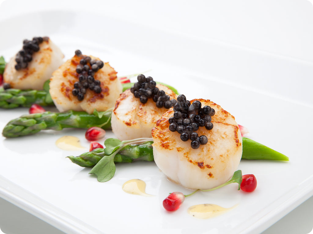 An appetizer of grilled sea scallops with Sevruga Caviar on top, served with asparagus and pomegranate seeds. 